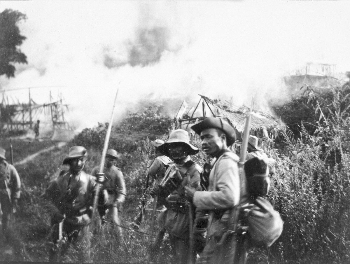 Una aldea Adi no identificada arde en el fondo de esta fotografía de miembros de un regimiento Gurkha tomada por DHR Gifford durante la Expedición Abor de 1911-12.