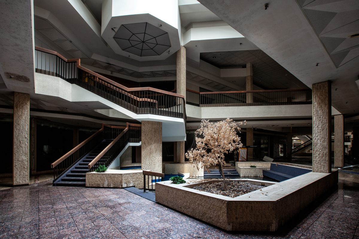 Una zona para sentarse y una escalera curva en el pasillo de un centro comercial en un lugar no revelado. 