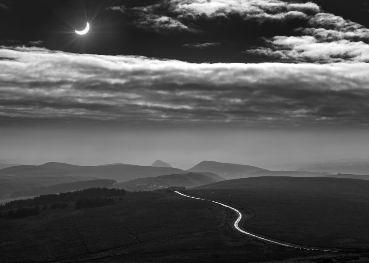 Un camino sinuoso en el Parque Nacional Peak District de Inglaterra marca el camino hacia un eclipse en progreso. ¿Qué camino tomarás para presenciar el próximo gran evento celestial?