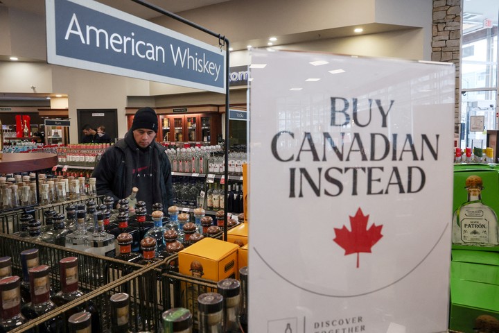 Un cliente sostiene una botella mientras se muestra un cartel que dice ''Buy Canadian Instead''  (Mejor compre canadiense) después de que las cinco principales marcas de licores estadounidenses fueran retiradas de la venta en las tiendas de licores de Columbia Británica, como parte de una respuesta a los aranceles del 25% del presidente estadounidense Donald Trump sobre los productos canadienses, en Vancouver, Columbia Británica, Canadá, 2 de febrero de 2025. REUTERS/Chris Helgren