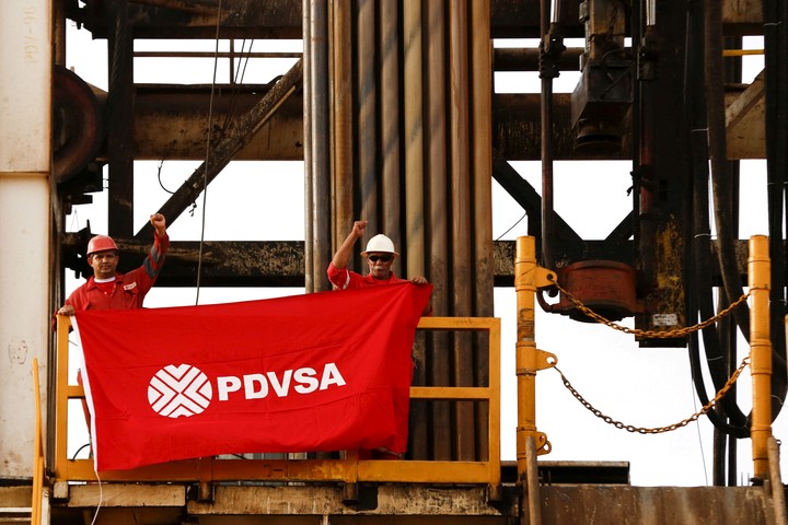 Trabajadores petroleros sostienen una bandera con el logotipo de la petrolera estatal venezolana PDVSA, en una plataforma de perforación en un pozo petrolero operado por ellos, en la faja petrolera del Orinoco. Foto Reuters