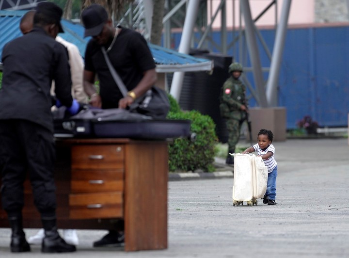 Un niño empuja una maleta hacia los agentes de seguridad ruandeses que controlan a las personas que cruzan desde el Congo en Gisenyi, Ruanda, el miércoles 29 de enero de 2025, tras los avances de los rebeldes del M23 en Goma, la capital del este del Congo. (AP Photo/Brian Inganga)