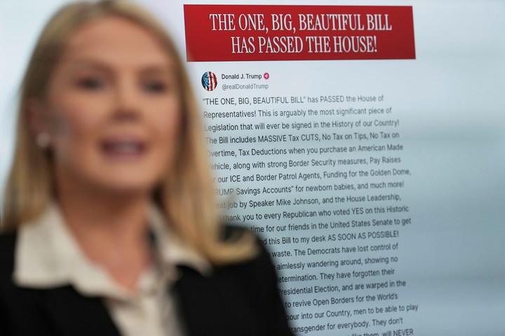 La secretaria de prensa de la Casa Blanca, Karoline Leavitt, habla con los periodistas mientras aparece en pantalla una imagen de la publicación del presidente Donald Trump en Truth Social sobre el paquete de recortes fiscales, en la sala de prensa James Brady de la Casa Blanca, el jueves 22 de mayo de 2025, en Washington. (AP Photo/Jacquelyn Martin)
