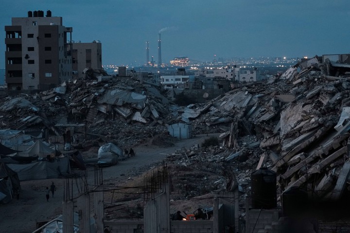 Palestinos desplazados por la ofensiva aérea y terrestre israelí sobre la Franja de Gaza permanecen rodeados de edificios destruidos durante el atardecer en una zona de la ciudad de Gaza, el lunes 2 de junio de 2025. (AP Photo/Jehad Alshrafi)