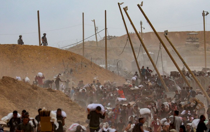 Soldados israelíes miran a los palestinos cargar alimentos en un centro de GHF. Foto: Reuters